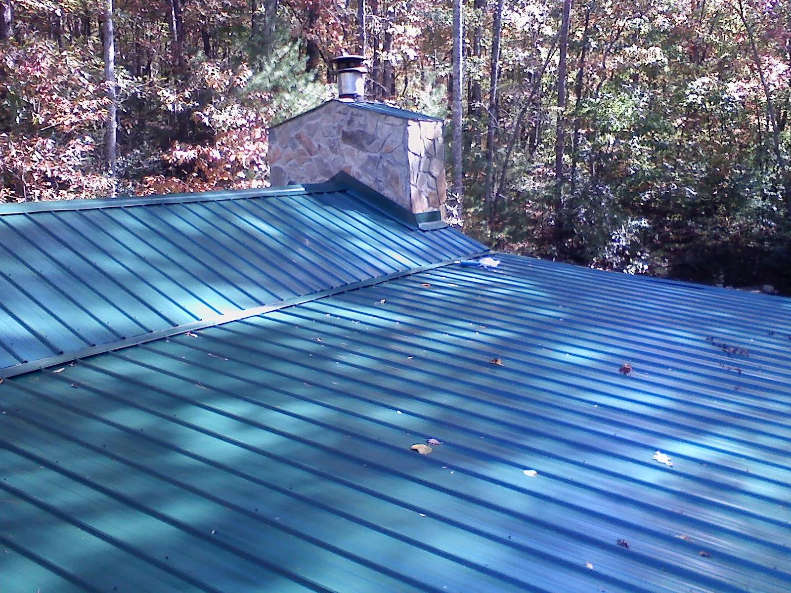 New green metal roof and stone chimney surrounded by autumn woods in Alexandria