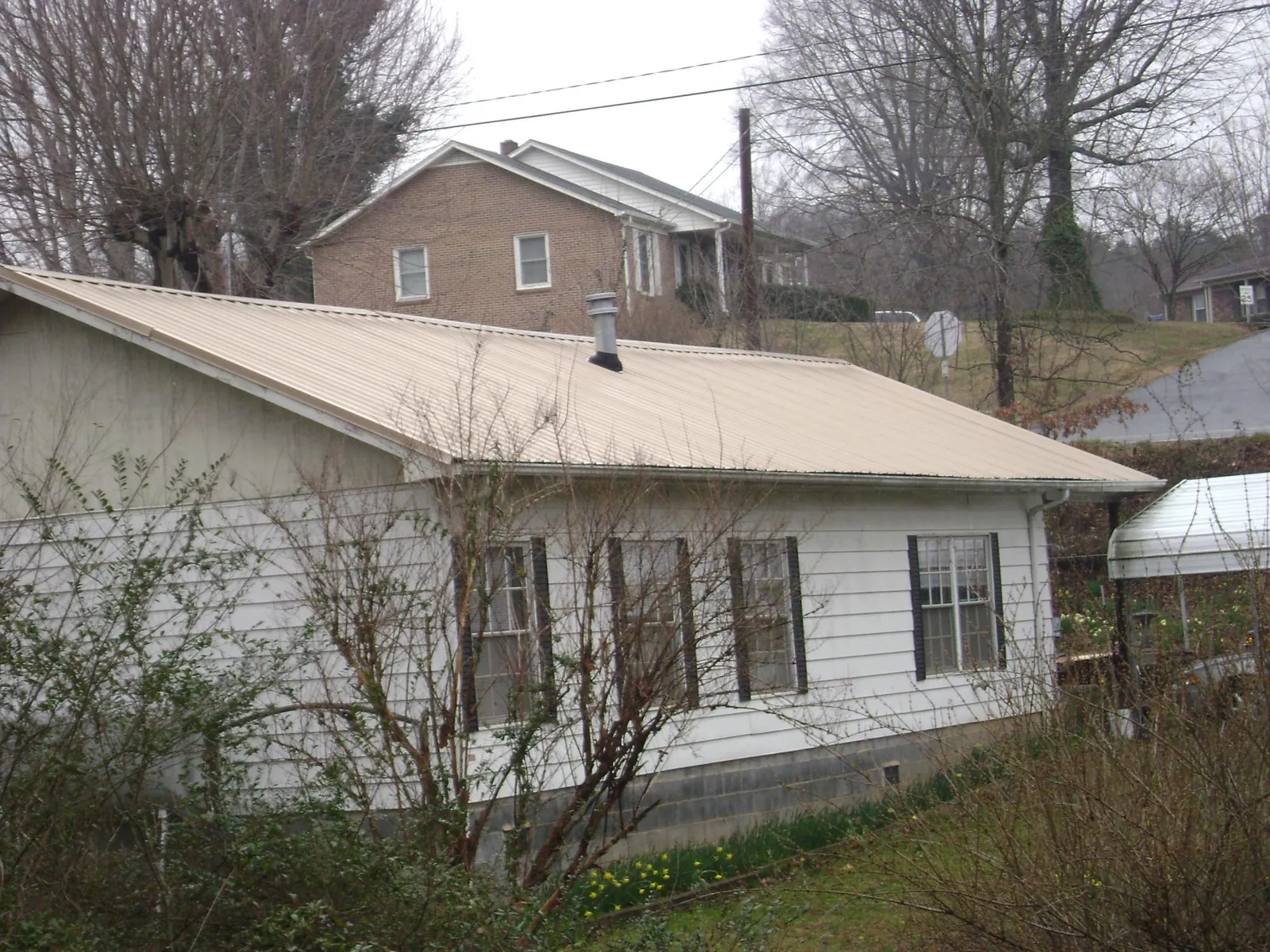 Tan metal roof on a white sided house set into a hillside — Commercial Roofing by Roofing Brothers in Alexandria
